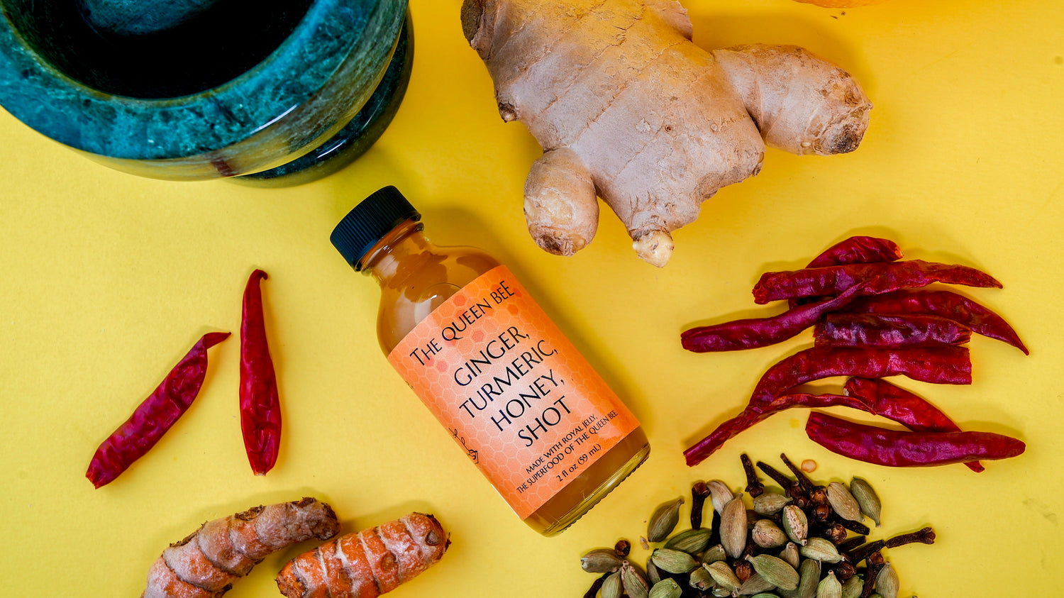 wellness shot surrounded with ingredients of ginger, cayenne, cardamom and turmeric